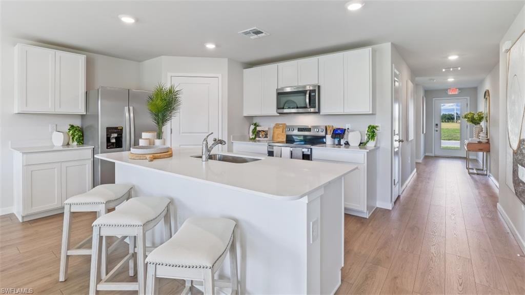 Model home. Kitchen with stainless steel appliances, white cabinetry, a kitchen bar, light wood-style floors, and recessed lighting