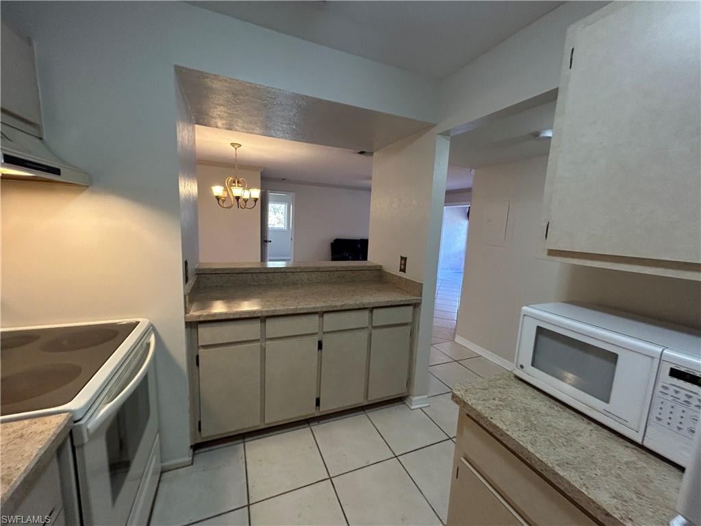 Kitchen with white appliances, hanging lights, light tile patterned flooring, and light stone counters