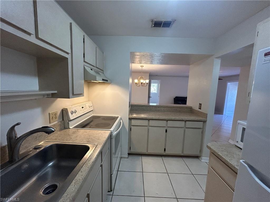 Kitchen featuring white appliances, gray cabinets, light tile patterned floors, and suspended lighting