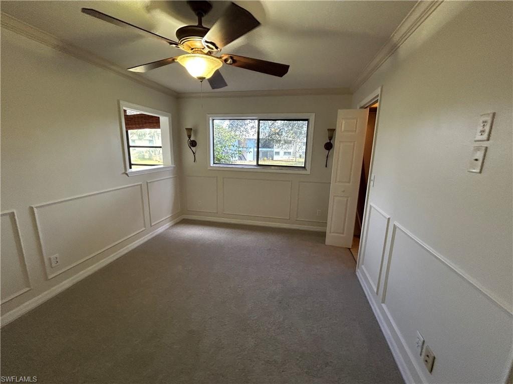 Carpeted empty room with a decorative wall, a ceiling fan, plenty of natural light, and ornamental molding