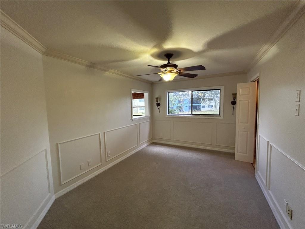 Carpeted spare room with a decorative wall, ceiling fan, ornamental molding, and wainscoting