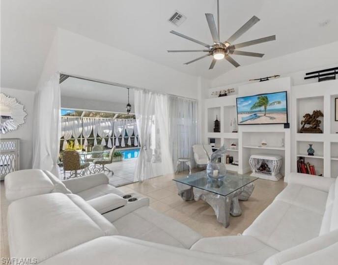 Tiled living room with built in features, a ceiling fan, and vaulted ceiling