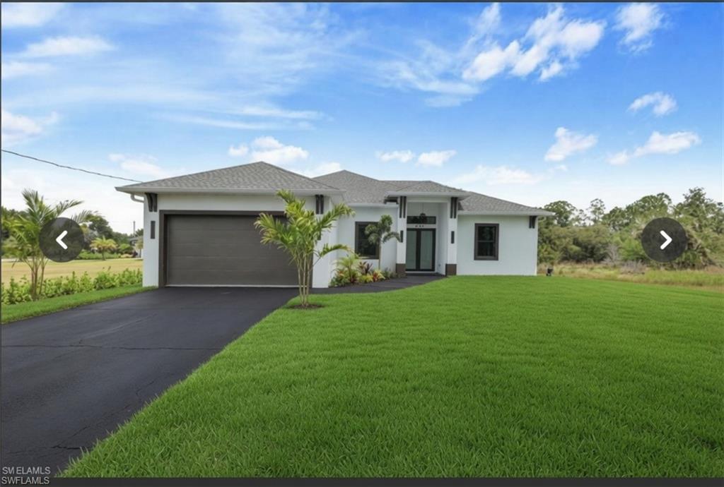 Contemporary single-story residence featuring a dark asphalt driveway, a two-car garage with a horizontally paneled door, a prominent covered entryway with a dark-framed door and sidelights, and a well-maintained front lawn with mature palm trees