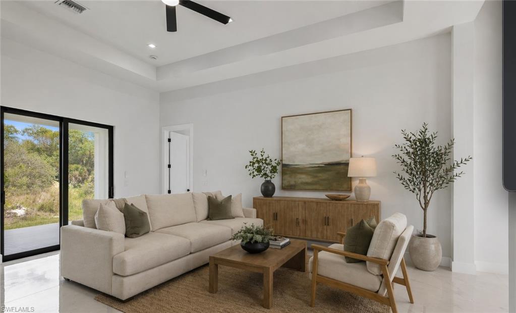 Spacious living area featuring a tray ceiling with recessed lighting and a ceiling fan, large sliding glass doors, and white tile flooring