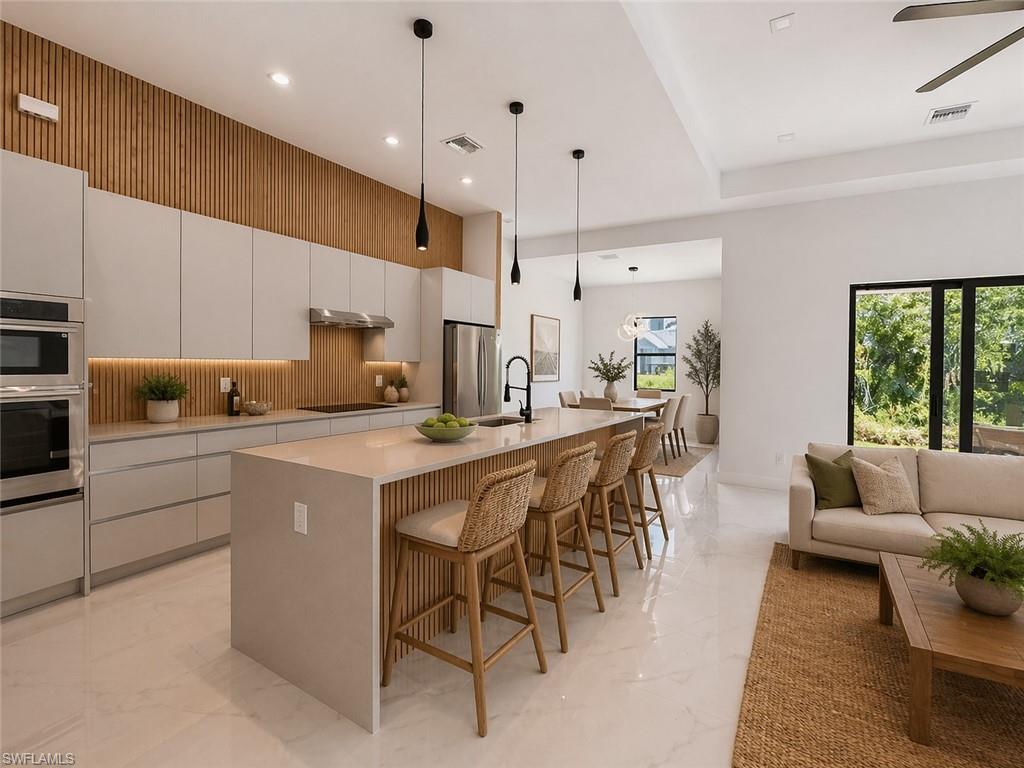 Open-concept living space featuring a gourmet kitchen with integrated appliances, a large center island with seating, a wood-slat accent wall, and recessed lighting