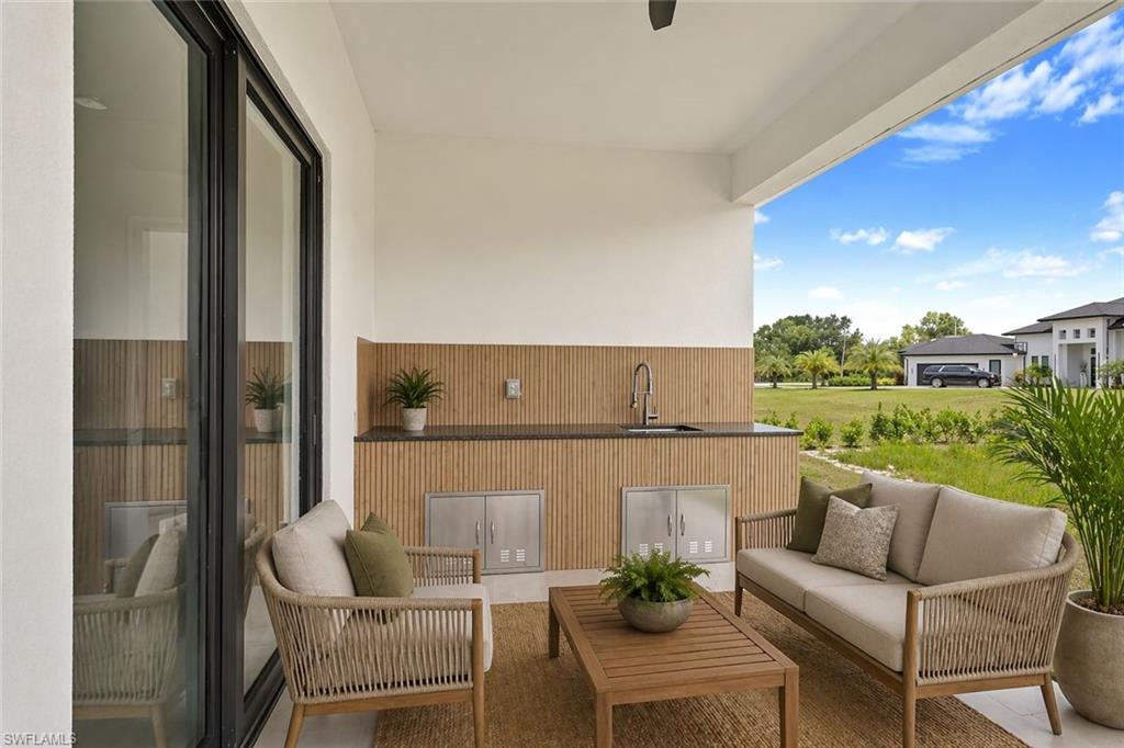 Covered outdoor kitchen featuring a dark countertop, stainless steel sink with a gooseneck faucet, and slatted wood-finish paneling