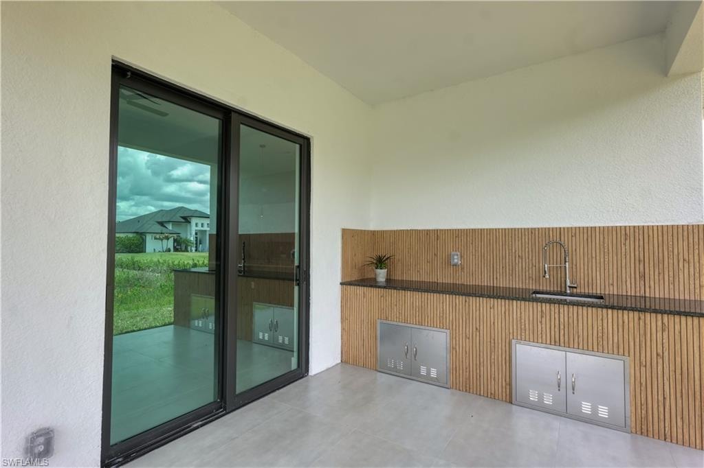 Covered outdoor kitchen featuring a built-in sink, stainless steel cabinetry, dark countertop, and wood-finish paneling