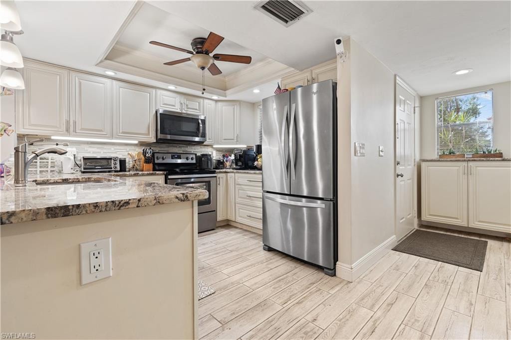 Kitchen with stainless steel appliances, light stone countertops, wood tiled floors, a ceiling fan, and a peninsula