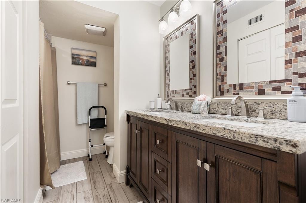 Full bathroom with double vanity, light wood finished floors, and curtained shower