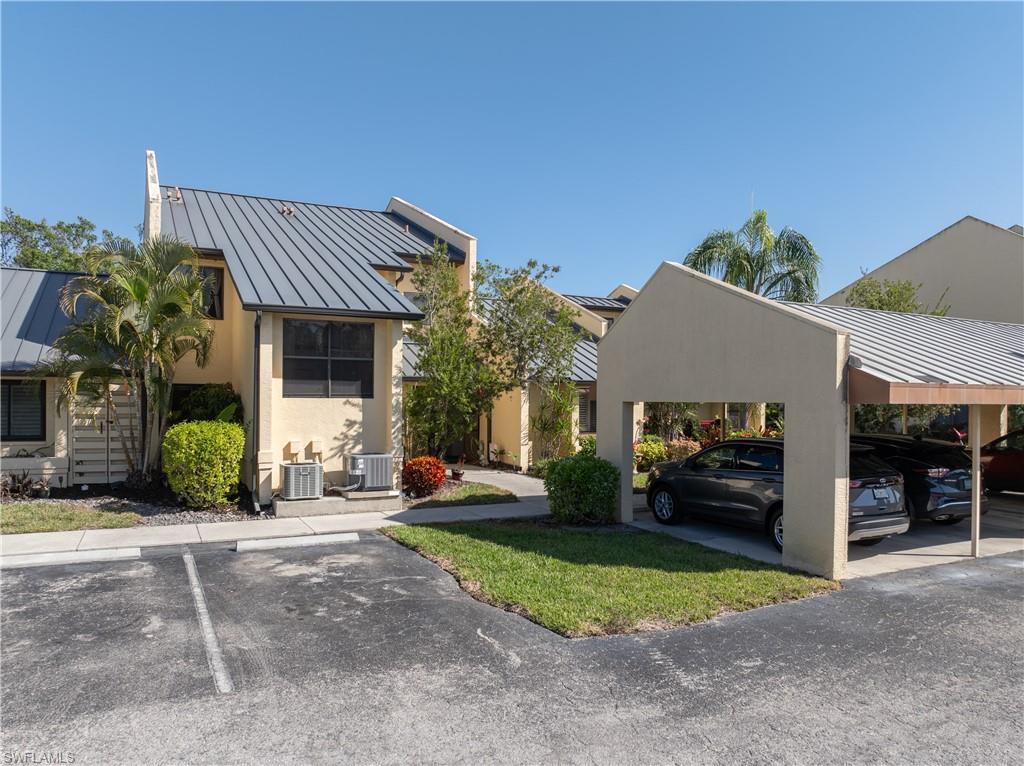 View of front of property with a standing seam roof, covered parking, stucco siding, and a front yard