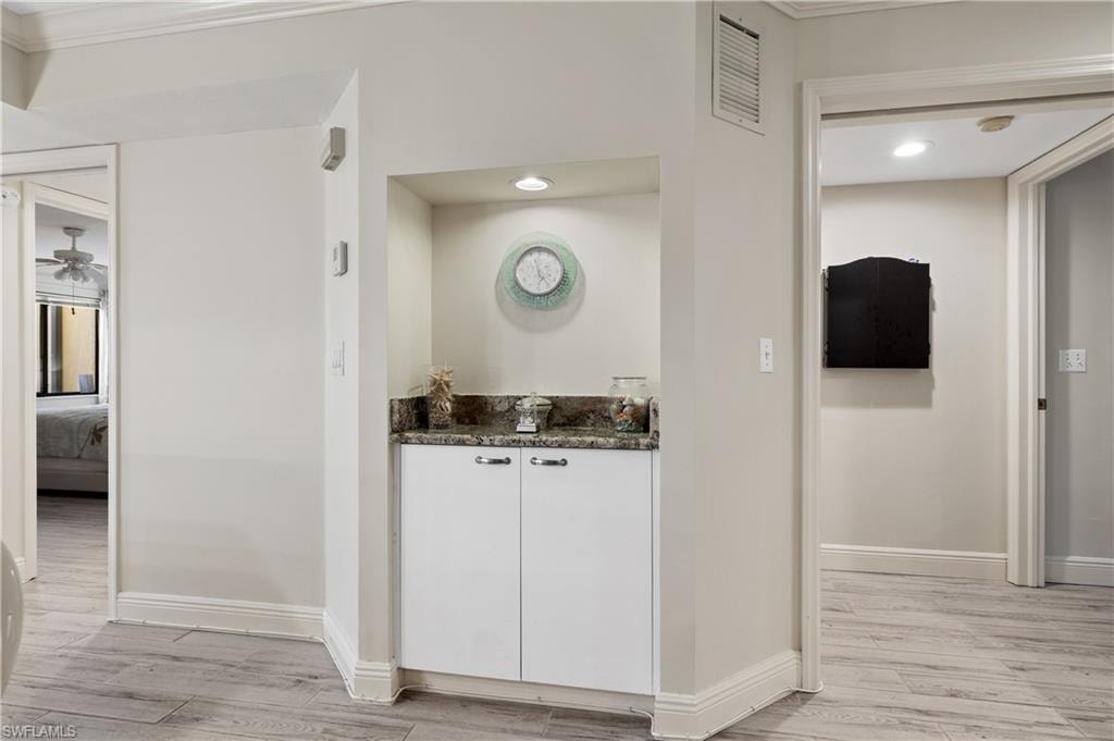 Bar featuring dark stone counters, light wood-style floors, a ceiling fan, white cabinets, and crown molding
