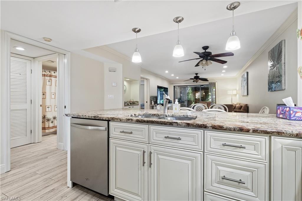 Kitchen featuring stainless steel dishwasher, a ceiling fan, light stone counters, open floor plan, and ornamental molding