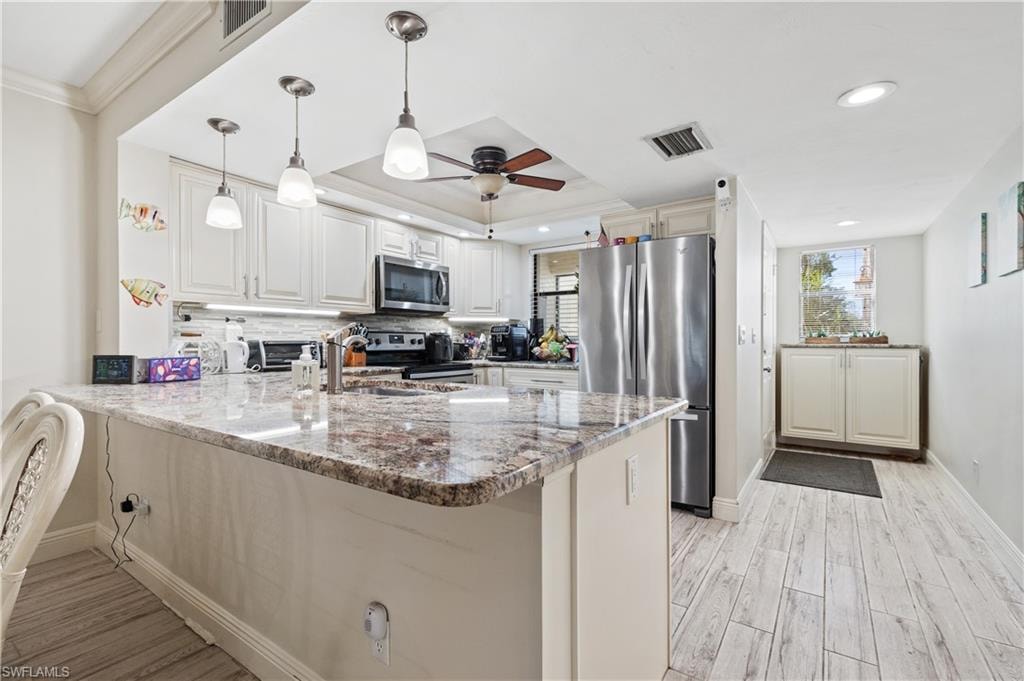 Kitchen featuring a peninsula, dark stone counters, stainless steel appliances, light wood-style flooring, and decorative light fixtures