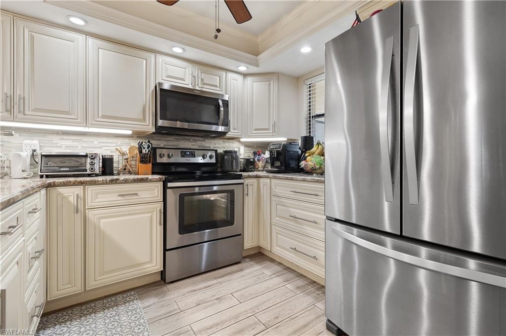 Kitchen with ornamental molding, stainless steel appliances, ceiling fan, wood finish floors, and light stone countertops