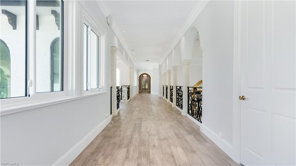 Hallway with arched walkways, light wood-style flooring, ornamental molding, and an upstairs landing