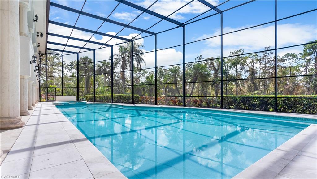 Combined pool / hot tub with glass enclosure, a sunroom, and a patio