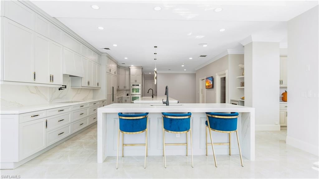 Kitchen featuring light stone counters, a breakfast bar area, crown molding, decorative backsplash, and hanging light fixtures