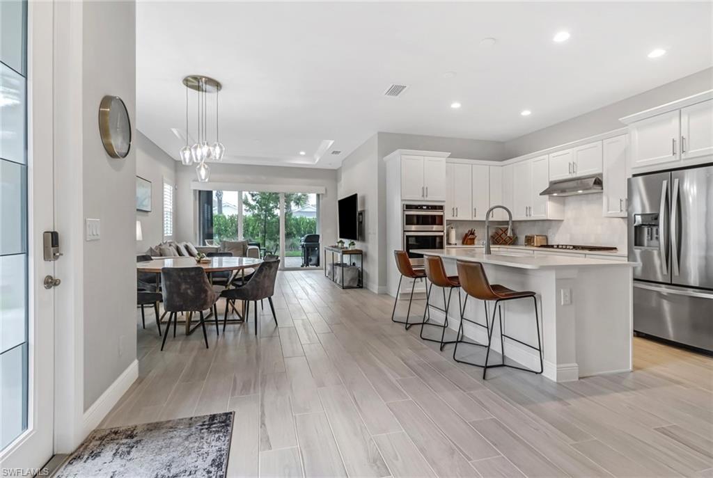 Kitchen featuring wood tiled floor, a breakfast bar, under cabinet range hood, appliances with stainless steel finishes, and backsplash