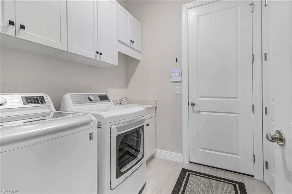 Laundry area featuring washer and clothes dryer, cabinet space, baseboards, and a sink