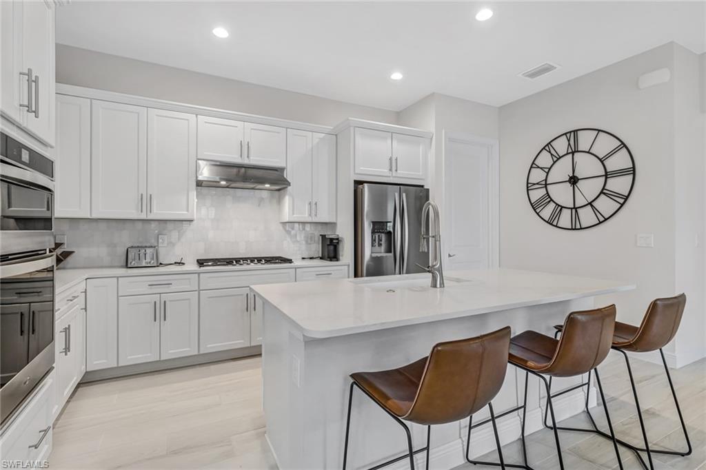 Kitchen with a breakfast bar area, stainless steel appliances, light countertops, under cabinet range hood, and backsplash