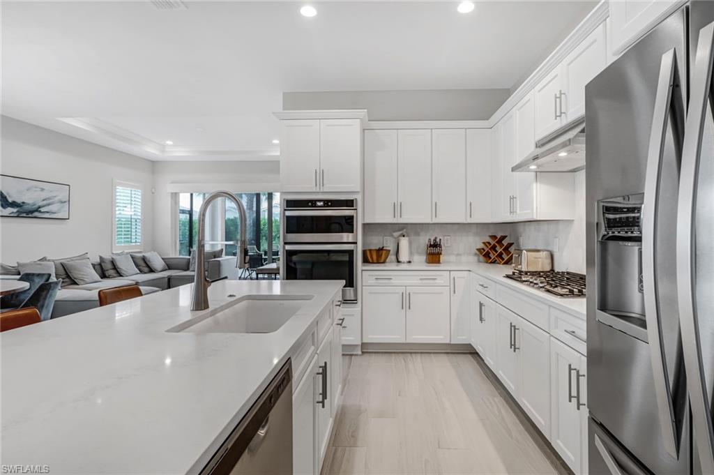 Kitchen with a sink, stainless steel appliances, under cabinet range hood, white cabinetry, and backsplash