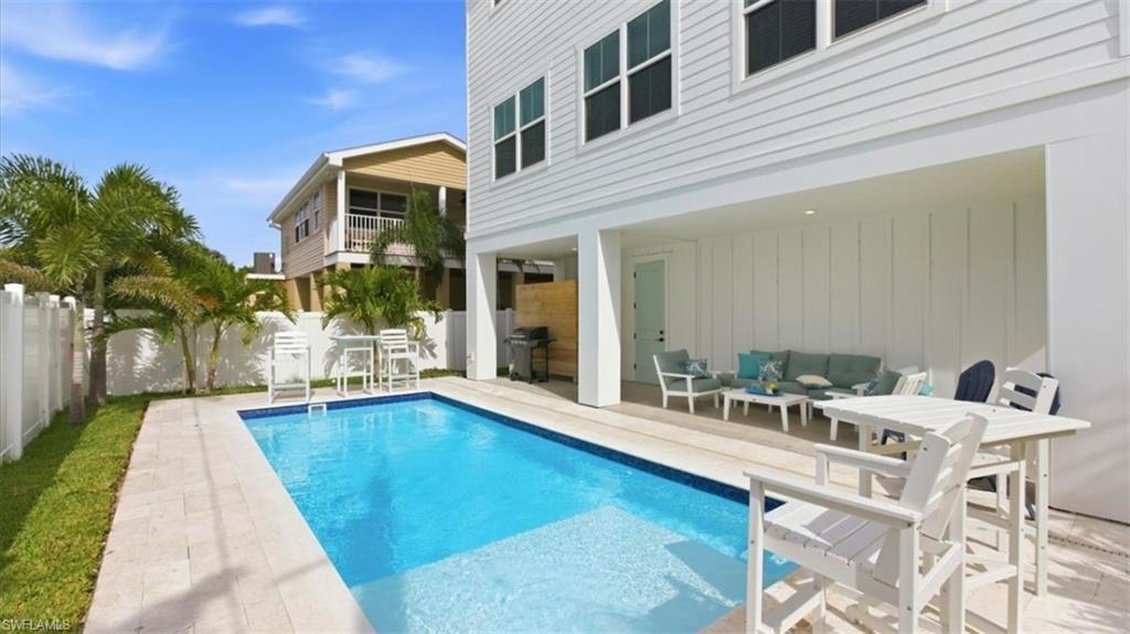 View of pool with a balcony, an outdoor lounge area, a fenced backyard, patio surround, and a grill - Virtually Edited