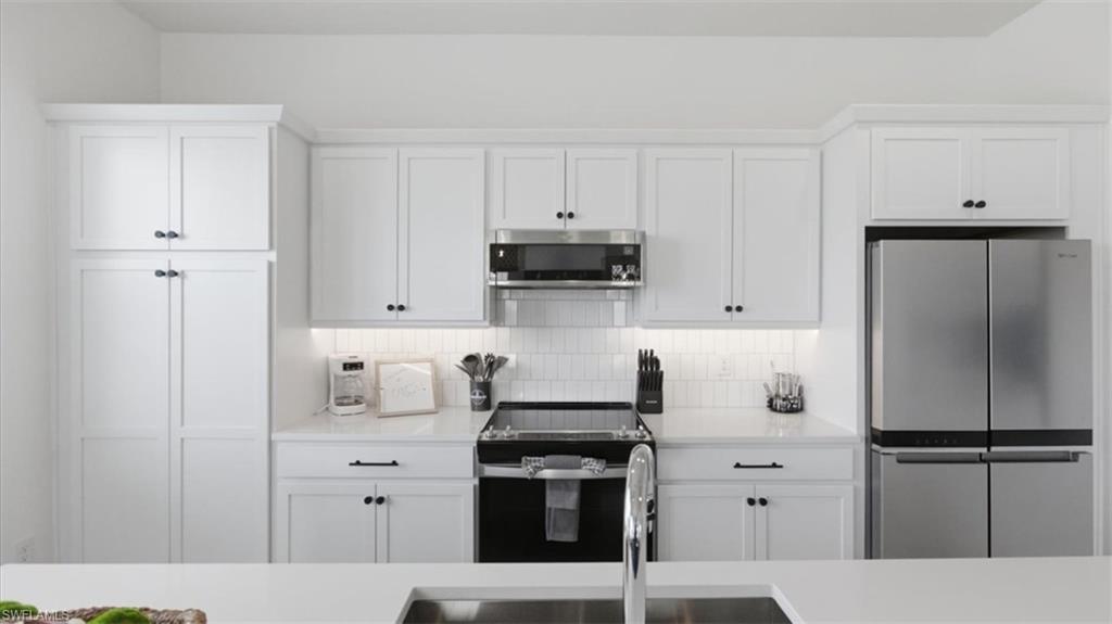Kitchen with stainless steel appliances, white cabinets, tasteful backsplash, and light stone counters - Virtually Edited