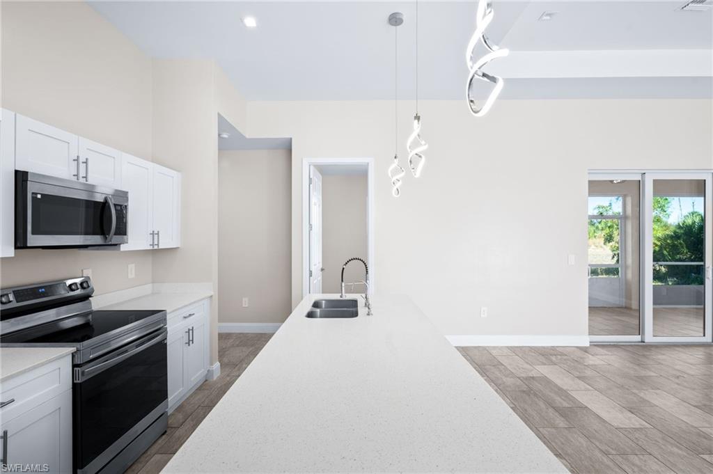 Kitchen featuring stainless steel appliances, hanging light fixtures, white cabinetry, light stone counters, and wood tiled floors