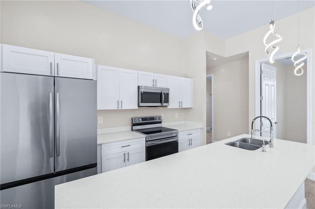 Kitchen featuring stainless steel appliances, white cabinetry, a center island with sink, hanging light fixtures, and light stone counters