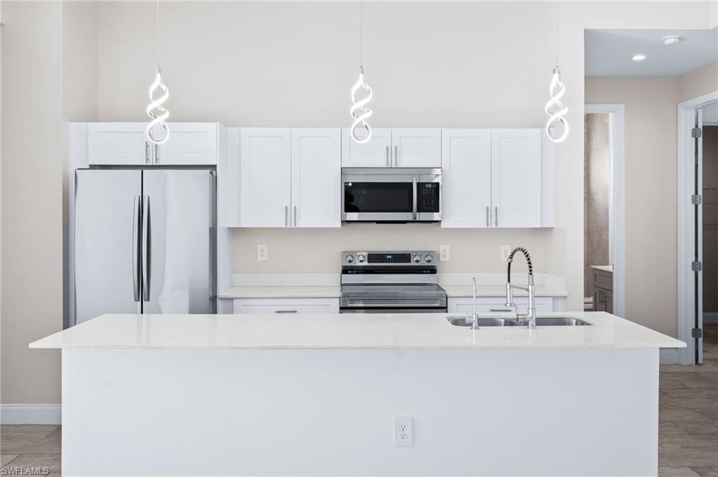 Kitchen with white cabinets, stainless steel appliances, light stone counters, and hanging light fixtures