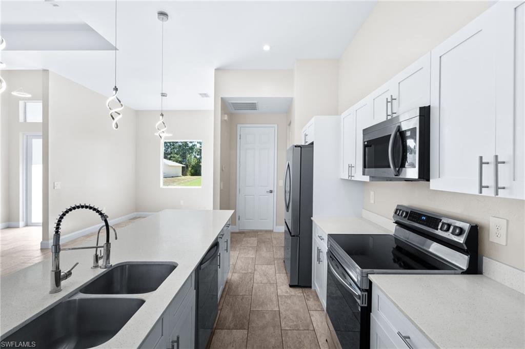 Kitchen featuring stainless steel appliances, white cabinets, light stone counters, and hanging light fixtures