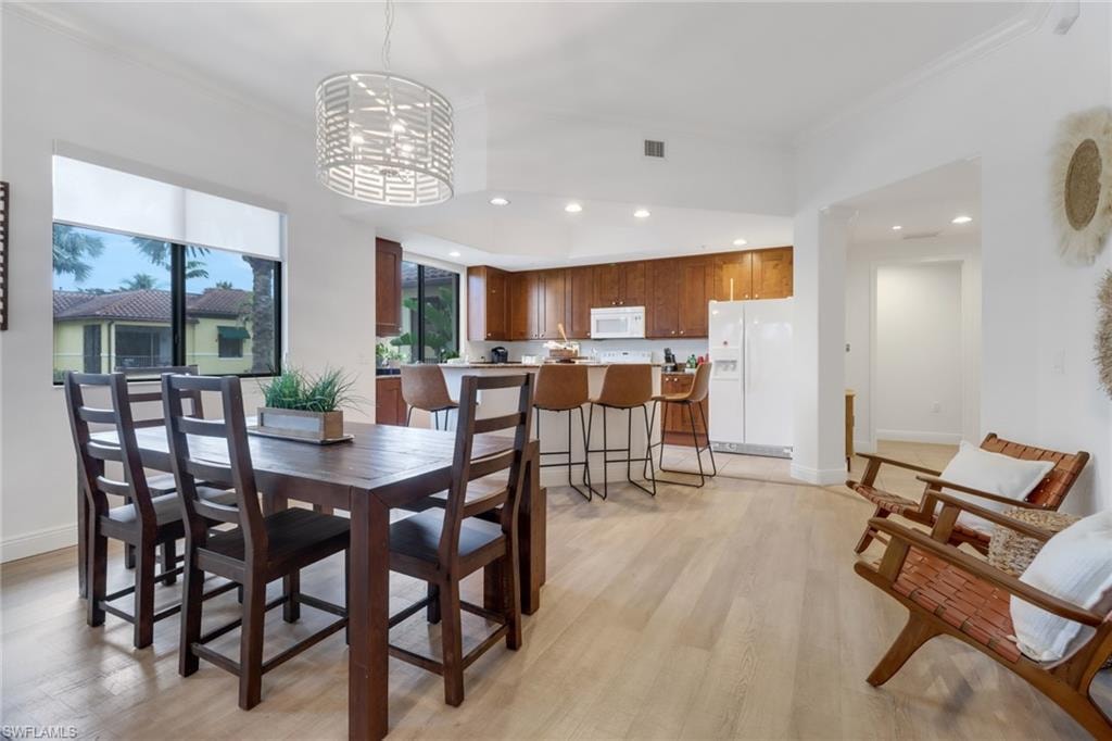 Dining room with light hardwood / wood-style flooring, ornamental molding, and a notable chandelier