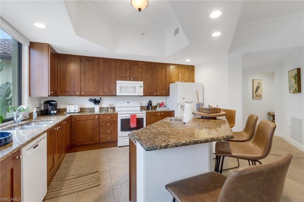 Kitchen with white appliances, a tray ceiling, sink, light tile patterned floors, and crown molding