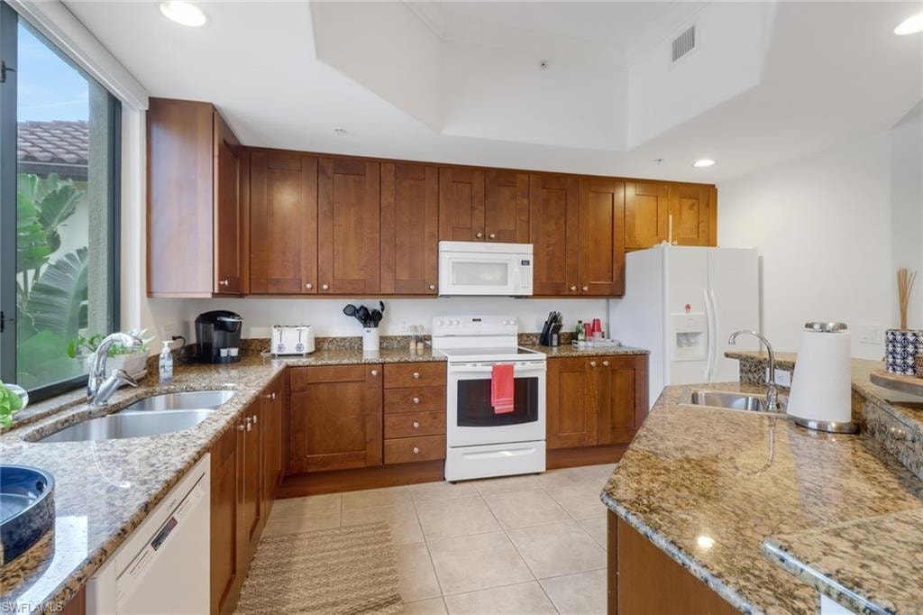 Kitchen featuring sink, white appliances, light tile patterned floors, and a raised ceiling