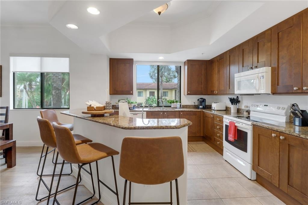Kitchen with a healthy amount of sunlight, light stone counters, a breakfast bar, and white appliances