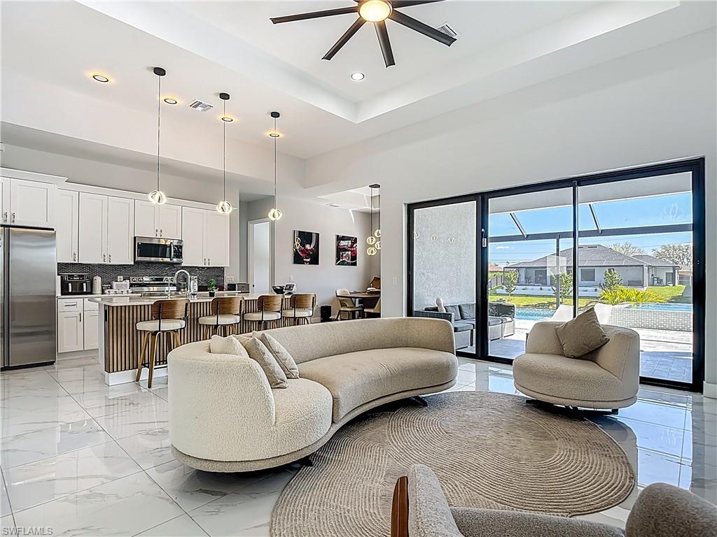 Living room featuring a ceiling fan, recessed lighting, light marble finish flooring, and a raised ceiling