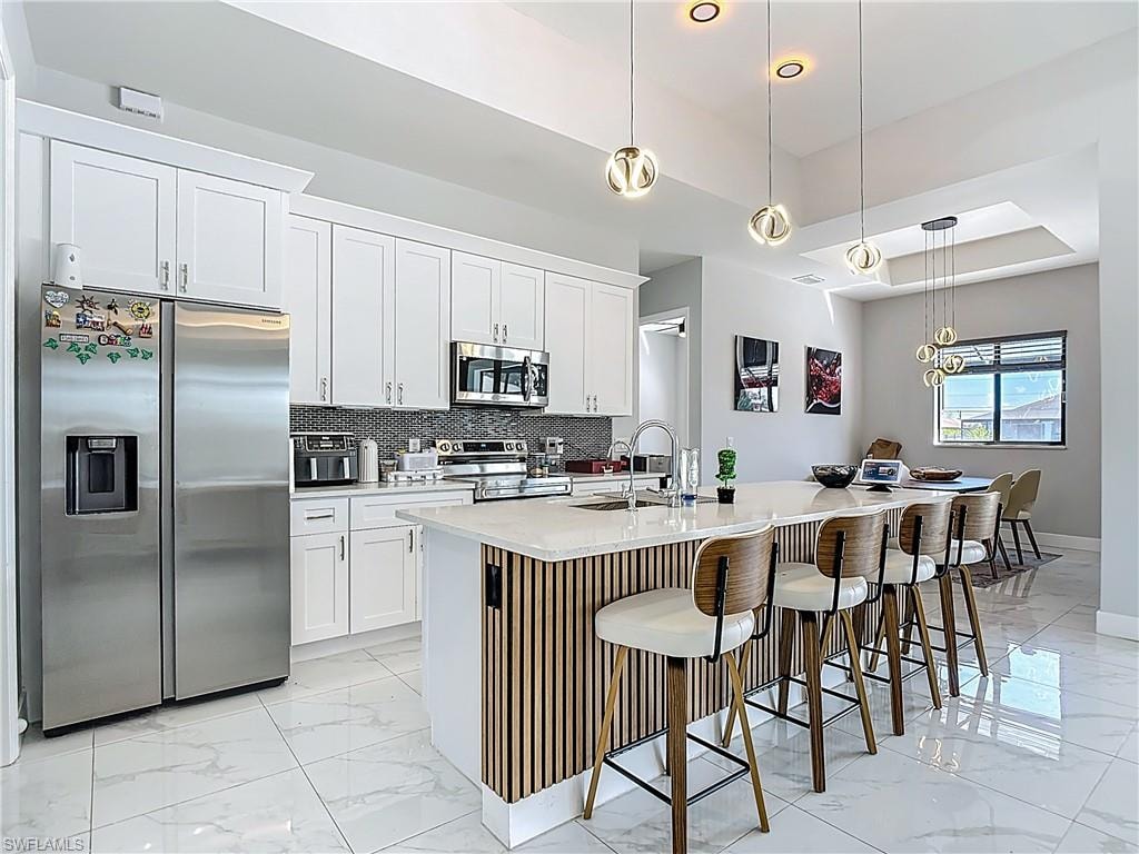 Kitchen with a breakfast bar area, pendant lighting, stainless steel appliances, a kitchen island with sink, and a tray ceiling