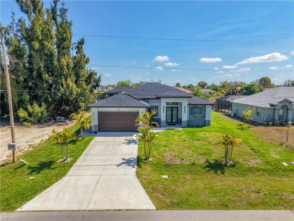 View of front facade featuring a front yard, driveway, a garage, stucco siding, and roof with shingles