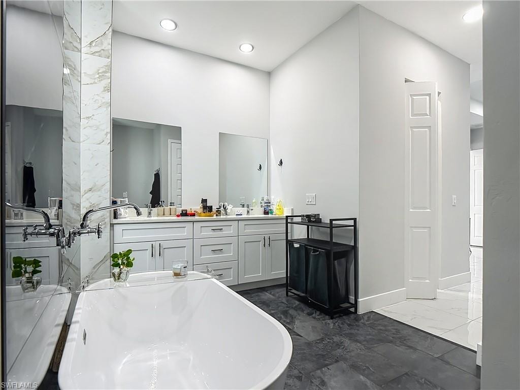 Full bathroom featuring double vanity, a freestanding tub, dark marble finish flooring, a high ceiling, and recessed lighting