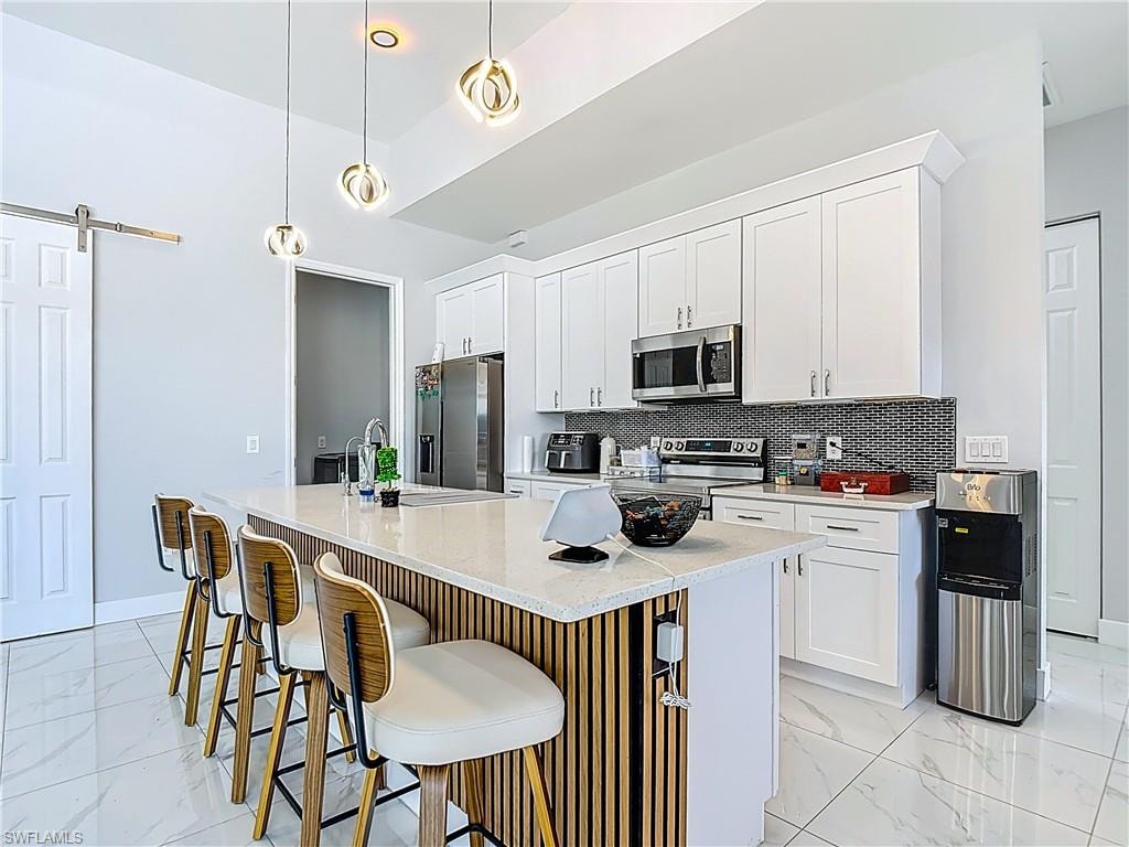 Kitchen featuring a barn door, white cabinetry, a kitchen bar, stainless steel appliances, and a center island with sink