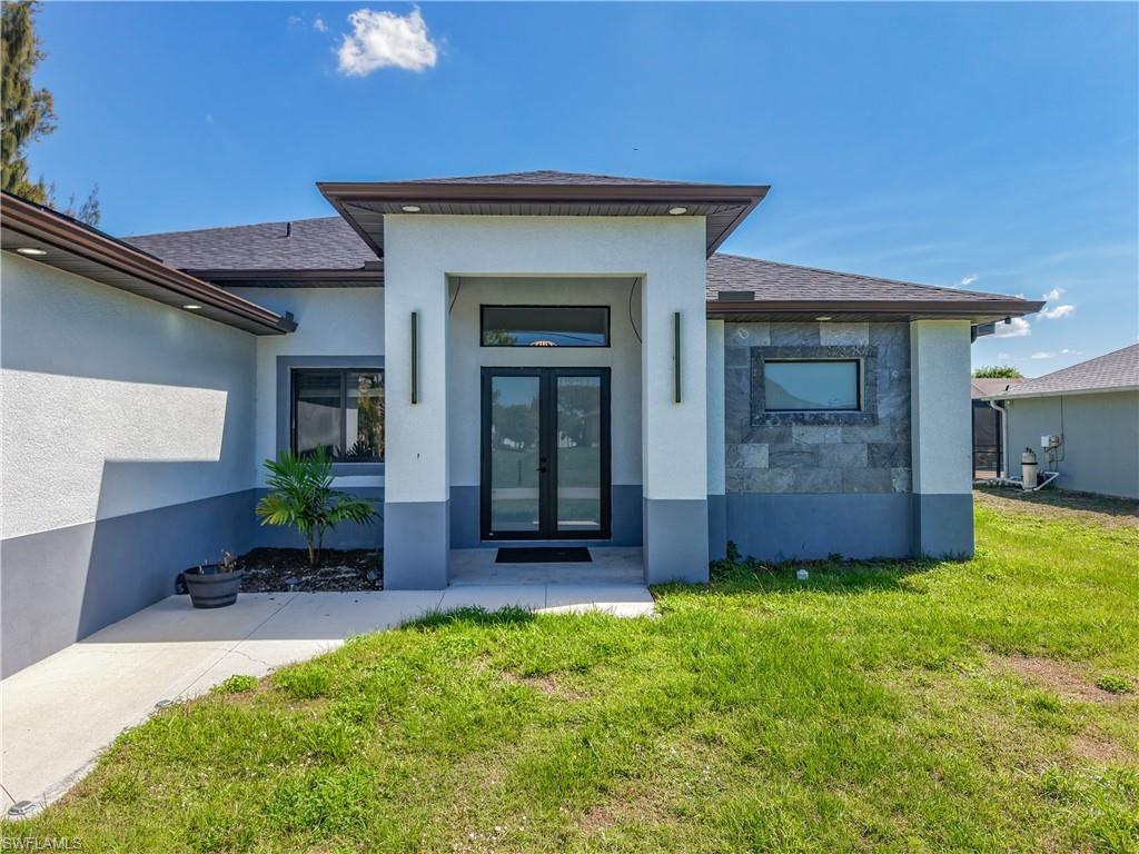 Doorway to property featuring french doors, a lawn, and stucco siding