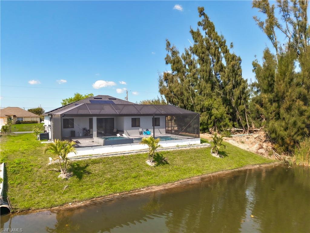 Back of property with an outdoor pool, a lawn, a water view, and a sunroom