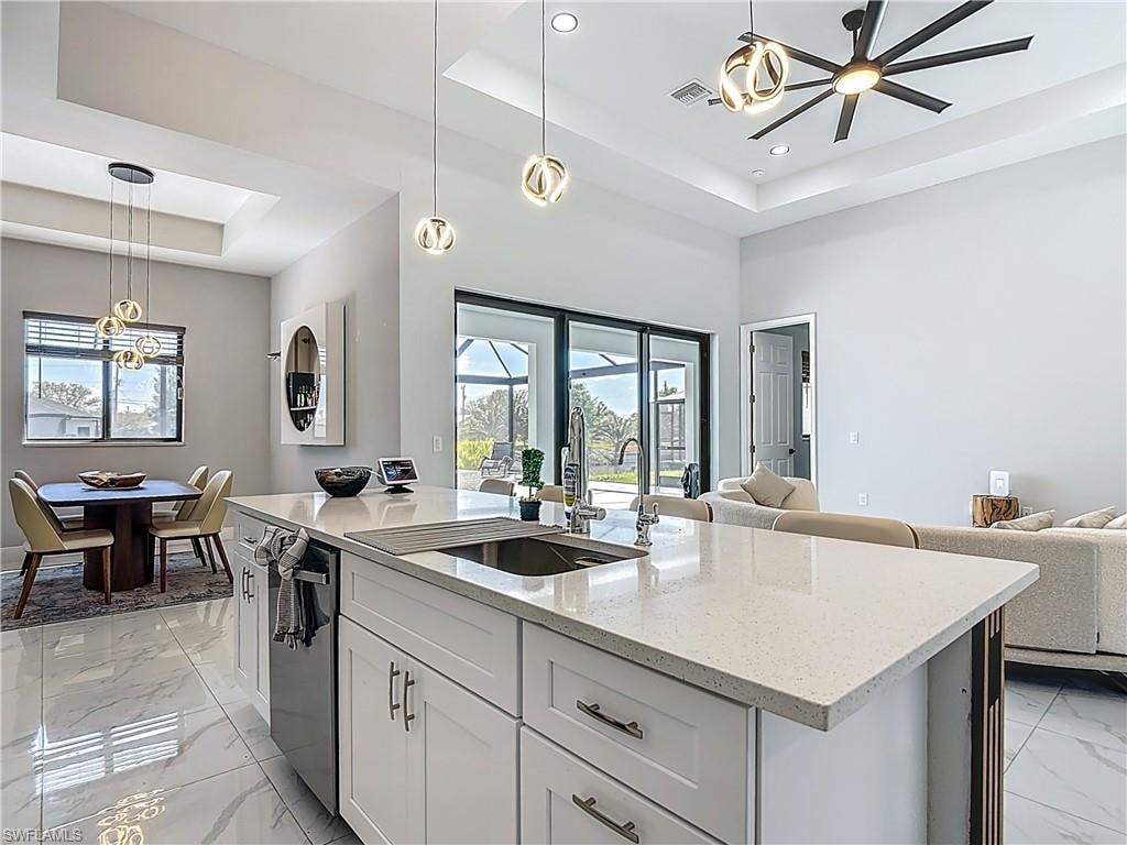 Kitchen with a tray ceiling, open floor plan, light marble finish floors, pendant lighting, and light stone countertops