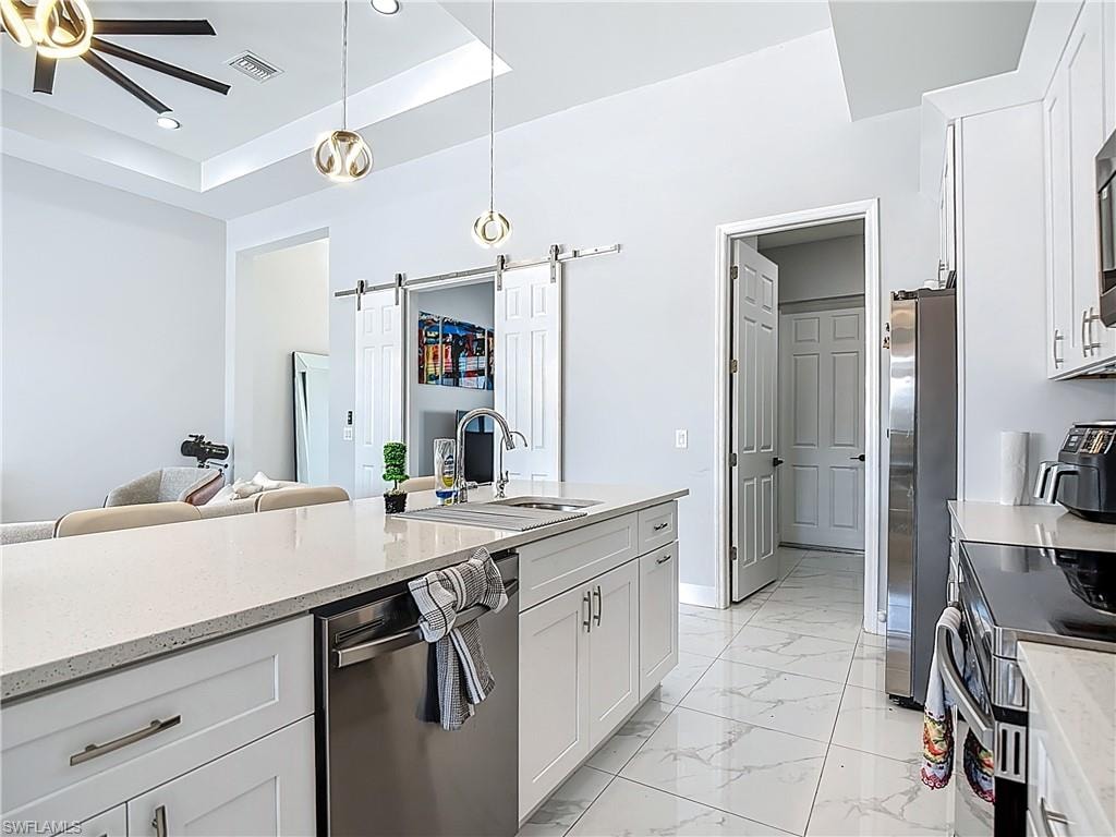 Kitchen with stainless steel appliances, white cabinetry, light marble finish floors, light stone counters, and a tray ceiling