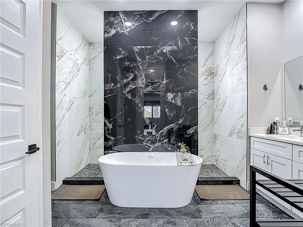 Bathroom with stone wall, tile walls, a freestanding bath, vanity, and a marble finish shower