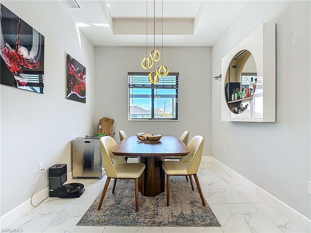 Dining space with light marble finish floors and a tray ceiling