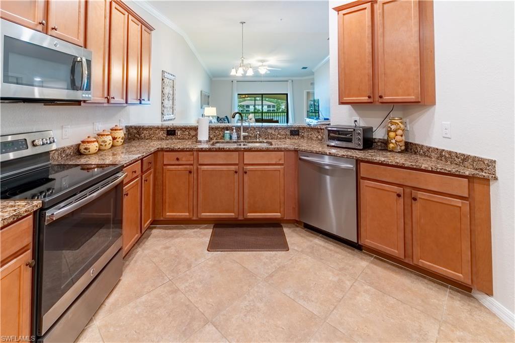 Kitchen with stainless steel appliances, sink, crown molding, vaulted ceiling, and an inviting chandelier