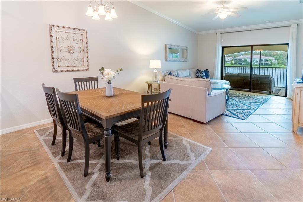 Tiled dining space featuring lofted ceiling, ceiling fan with notable chandelier, and crown molding