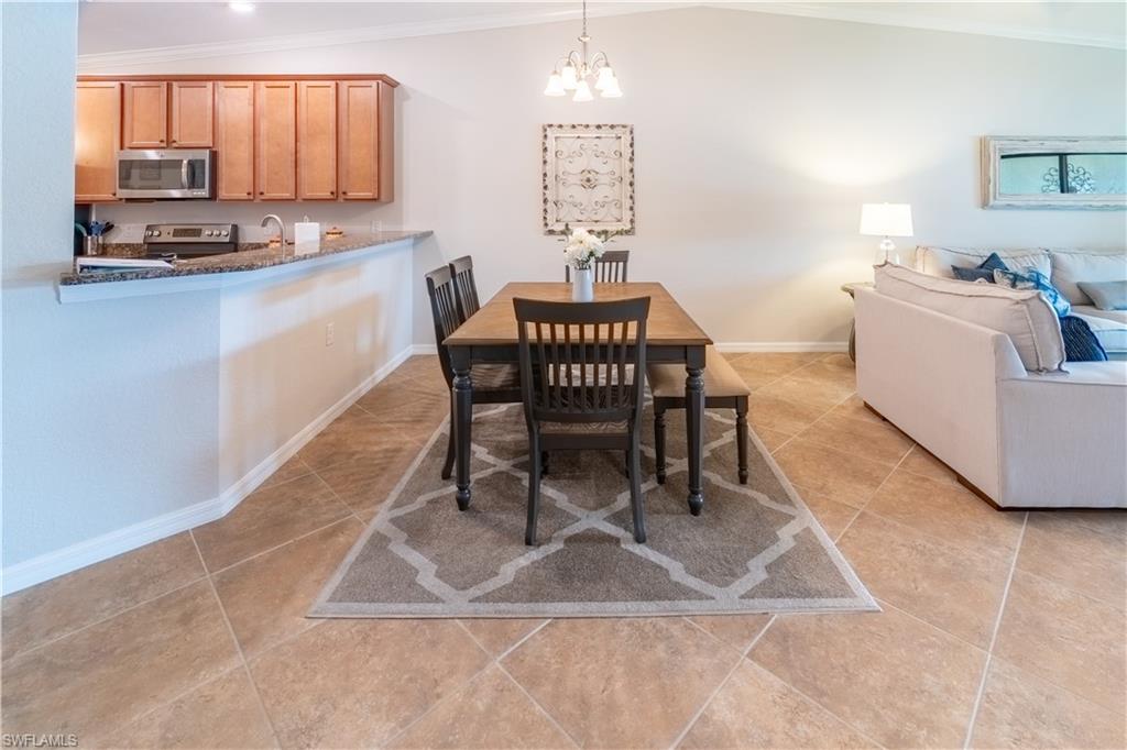 Tiled dining area with lofted ceiling, crown molding, an inviting chandelier, and sink