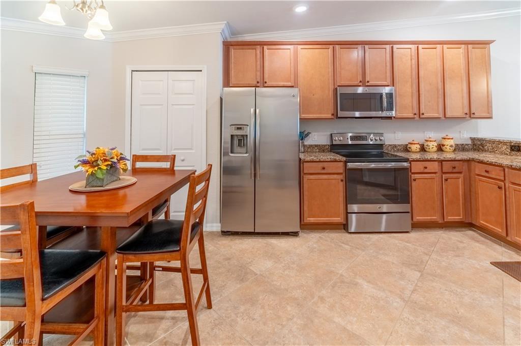 Kitchen featuring stone counters, stainless steel appliances, vaulted ceiling, crown molding, and a notable chandelier